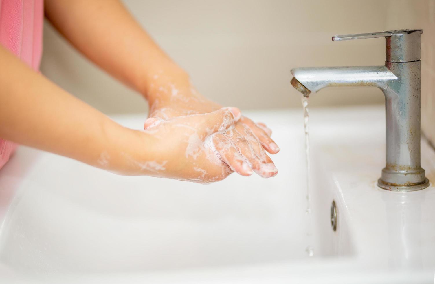 Hygiene. Cleaning Hands. Washing hands with soap. Young woman washing hands with soap over sink in bathroom, closeup. Covid19. Coronavirus. photo