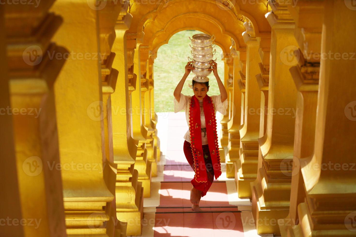 Young Asian girl in traditional Burmese costume holding bowl of rice on hand at golden pagoda in Myanmar temple. Myanmar women holding flowers with Burmese traditional dress visiting a Buddhist temple photo