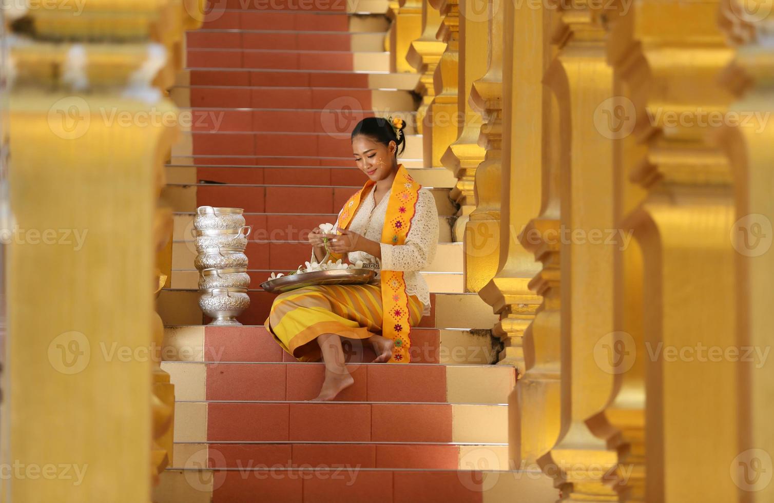 Young Asian girl in traditional Burmese costume holding bowl of rice on hand at golden pagoda in Myanmar temple. Myanmar women holding flowers with Burmese traditional dress visiting a Buddhist temple photo