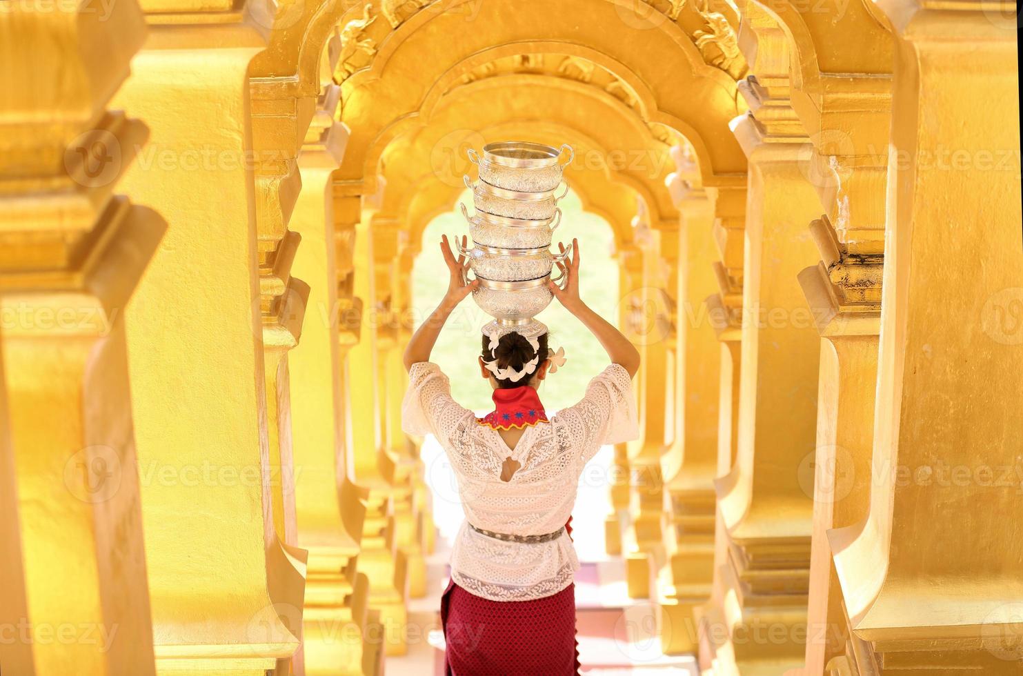 joven asiática con traje tradicional birmano sosteniendo un tazón de arroz a mano en la pagoda dorada en el templo de myanmar. mujeres de myanmar sosteniendo flores con vestido tradicional birmano visitando un templo budista foto