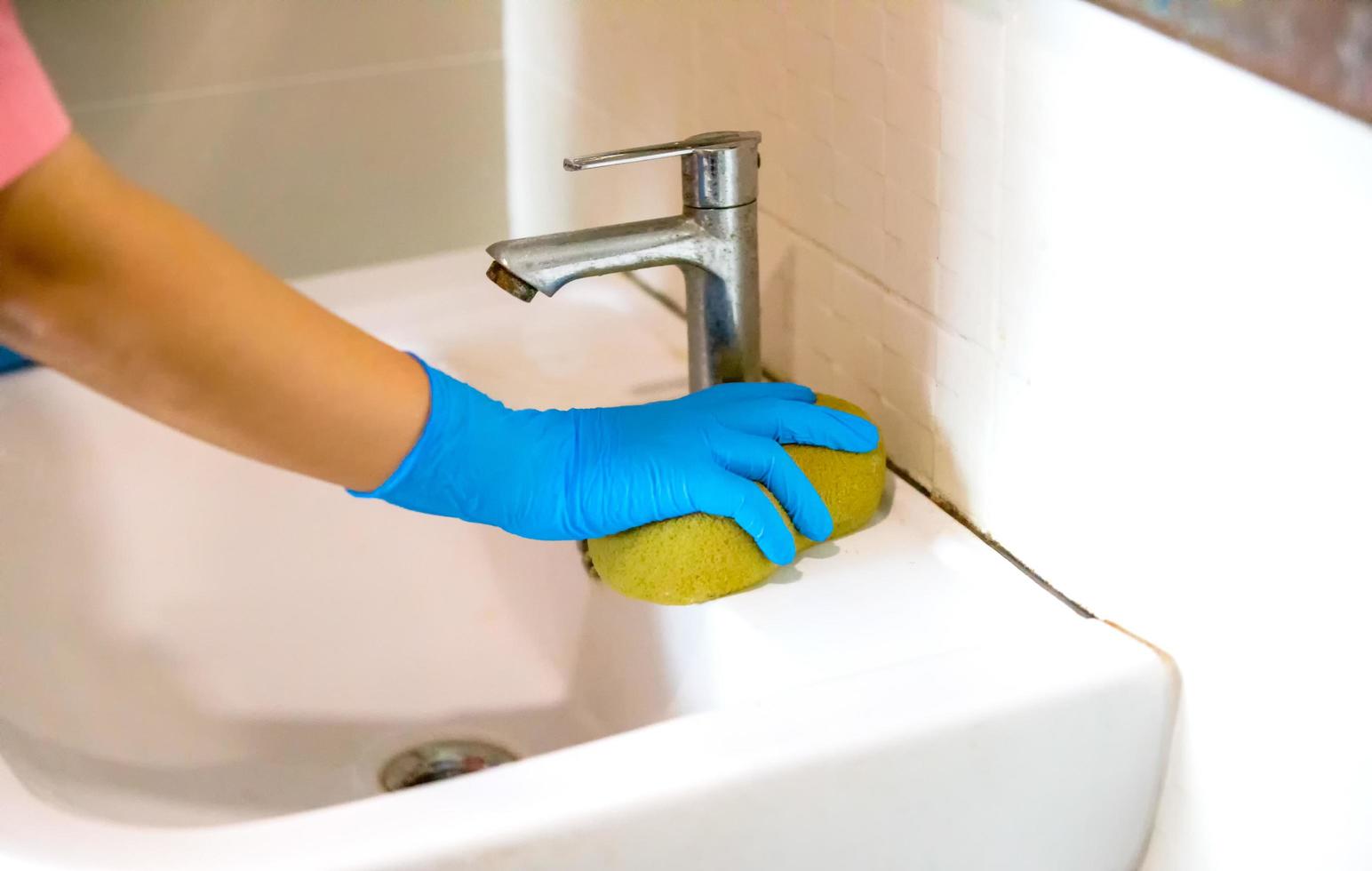 Person, a hand in a blue rubber glove in the picture, removes and washes bathroom sink photo