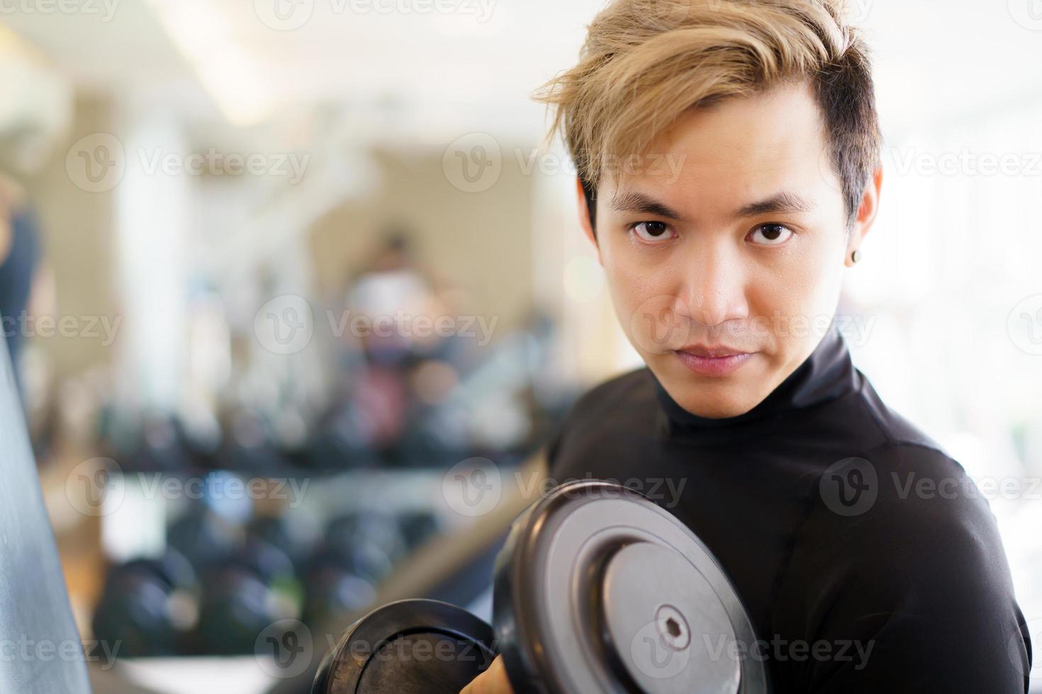 un joven apuesto asiático haciendo un entrenamiento con pesas usando pesas en el gimnasio. foto
