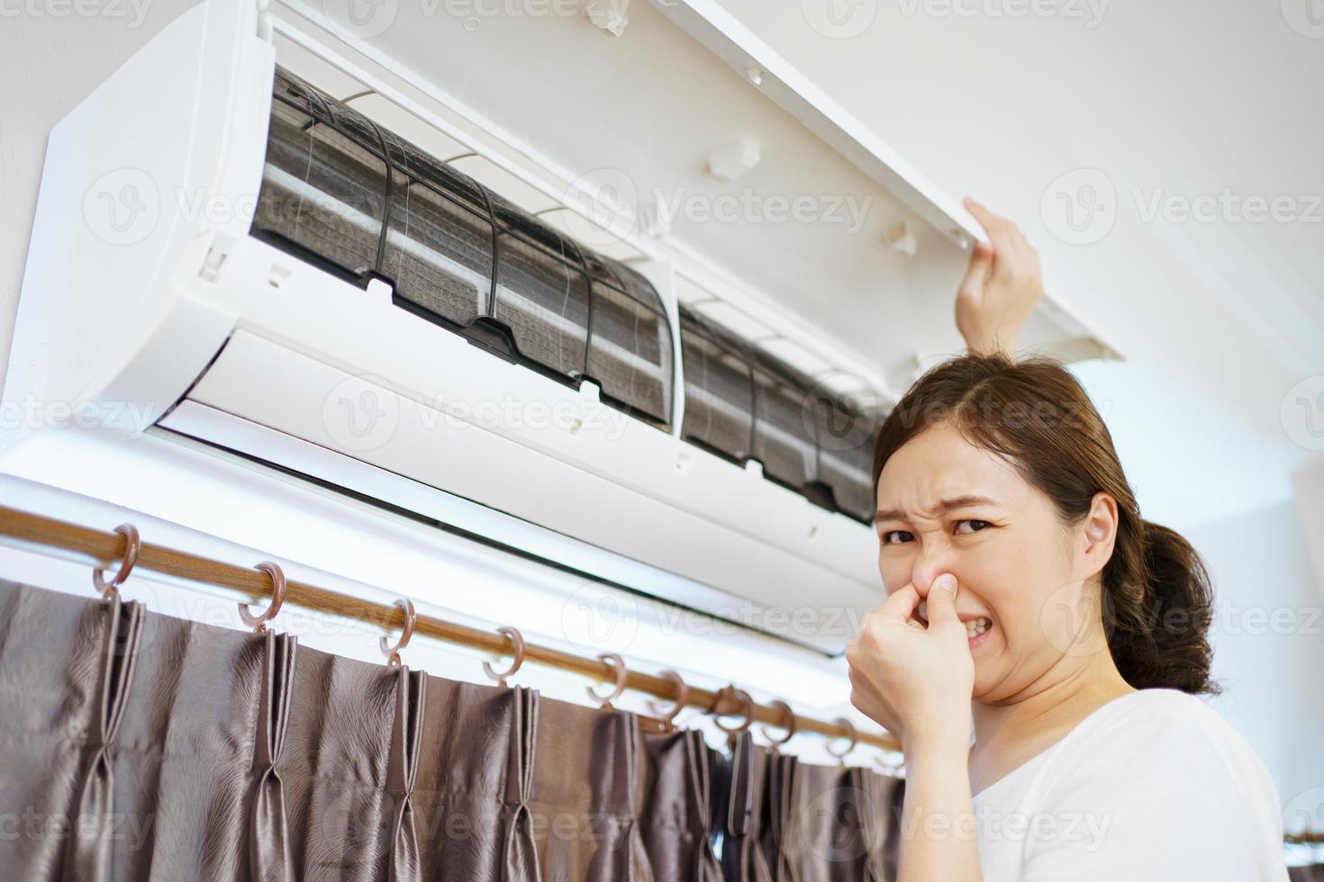 Asian woman cleaning a dirty and dusty air conditioning filter in her house. Housewife removing a dusty air conditioner filter. photo