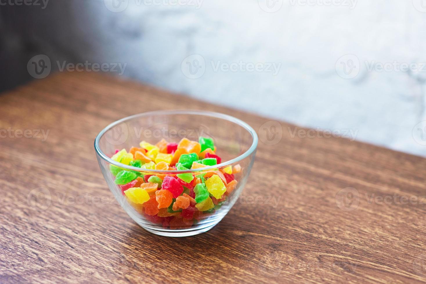 Multicolored candied fruit in a glass vase on table. photo
