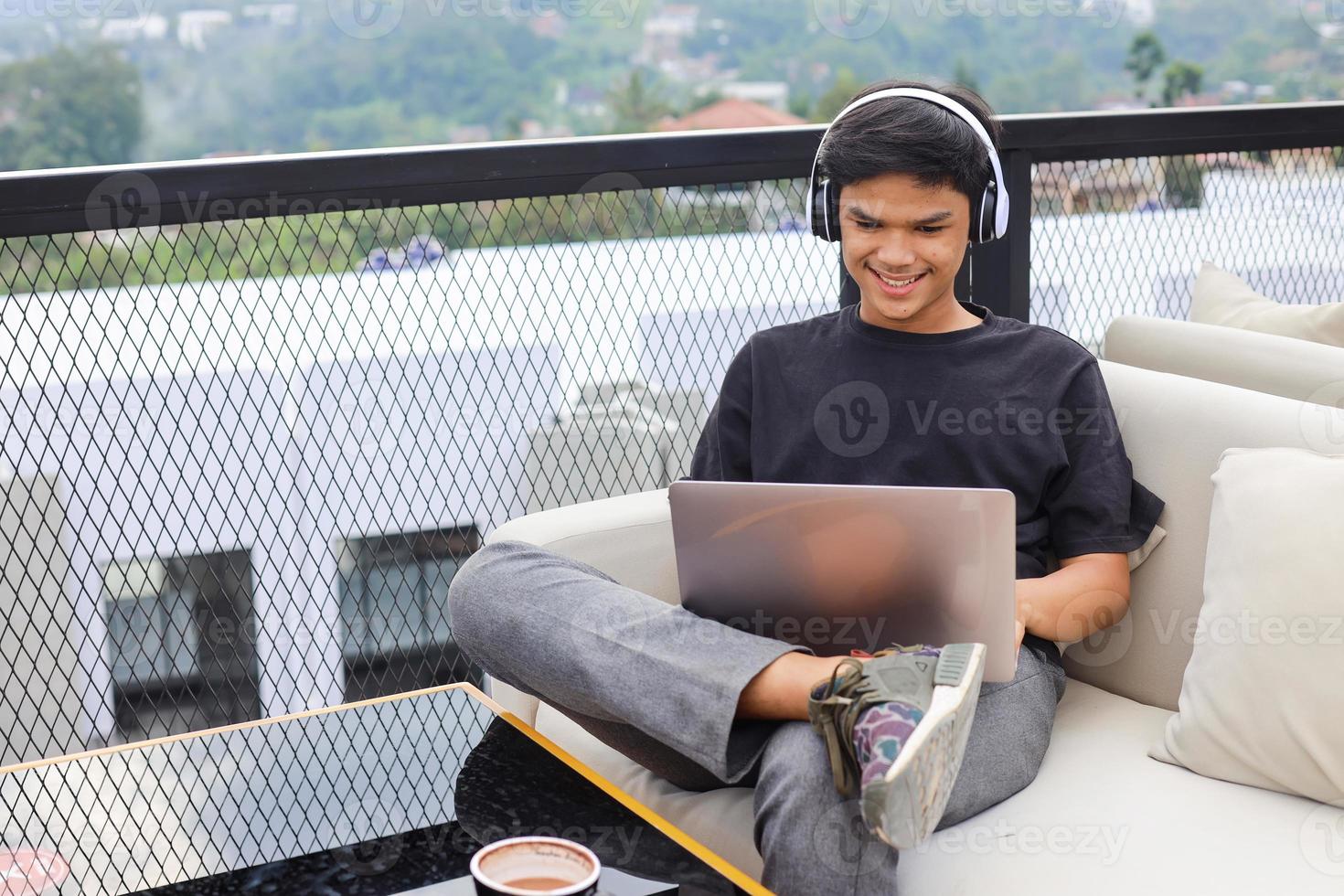 Asian male student relaxing on couch while studying online using laptop and headphone photo