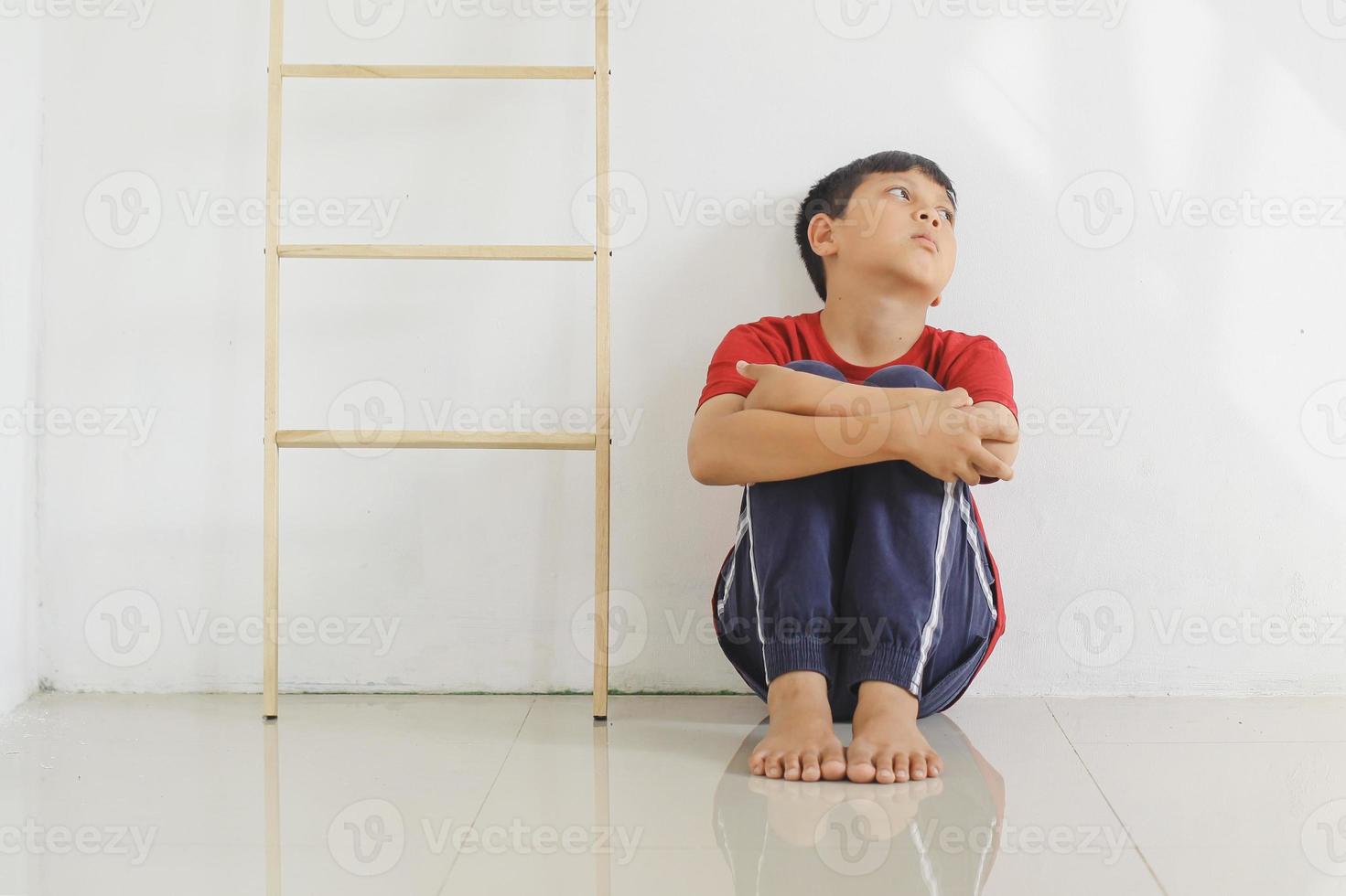 niño triste y solitario sentado en el suelo contra la pared. experiencia traumática infantil, psicología psicológica, síndrome de asperger, trastorno de asperger, autista, autismo. foto