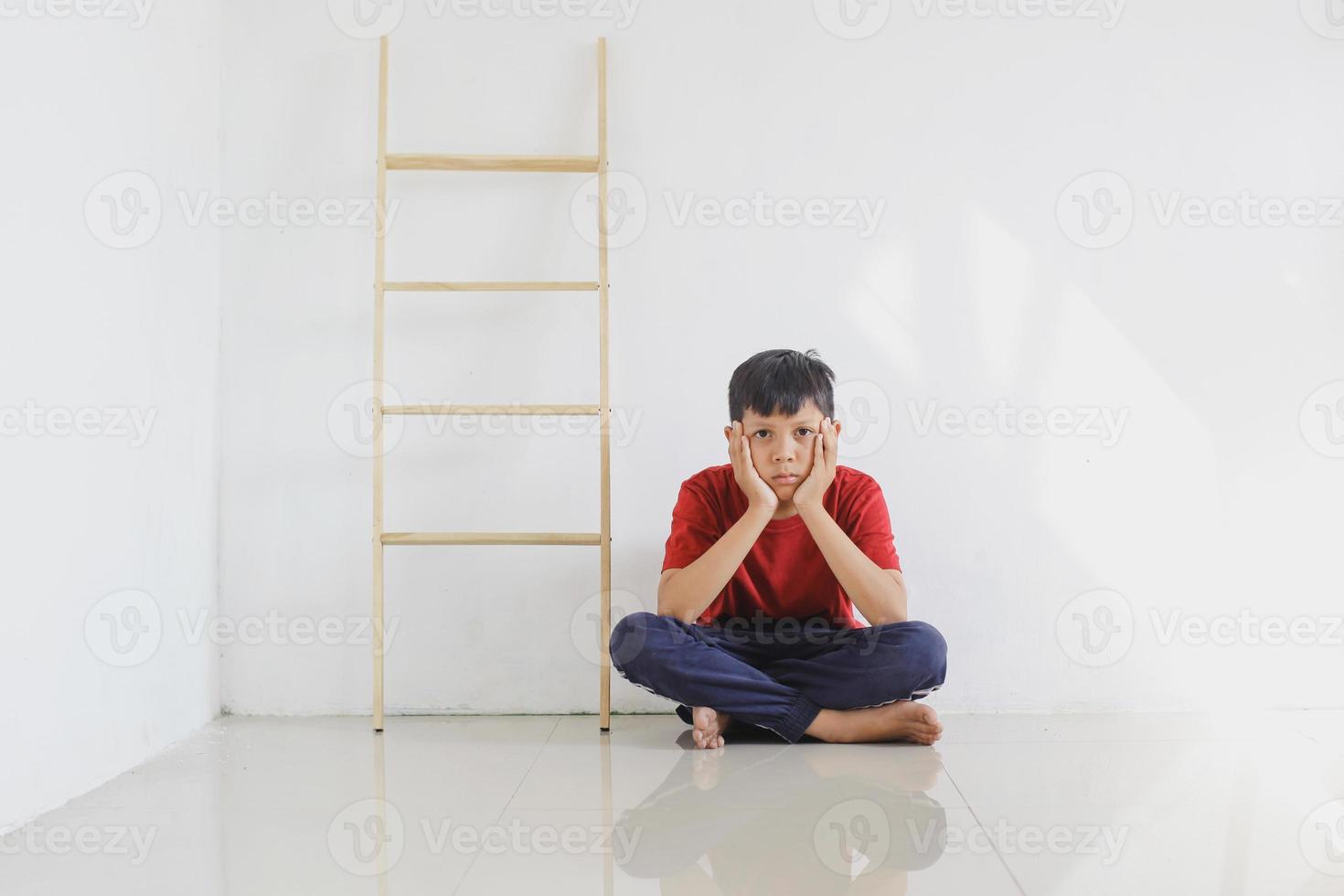 Sad and lonely child sitting alone on the floor against the wall photo
