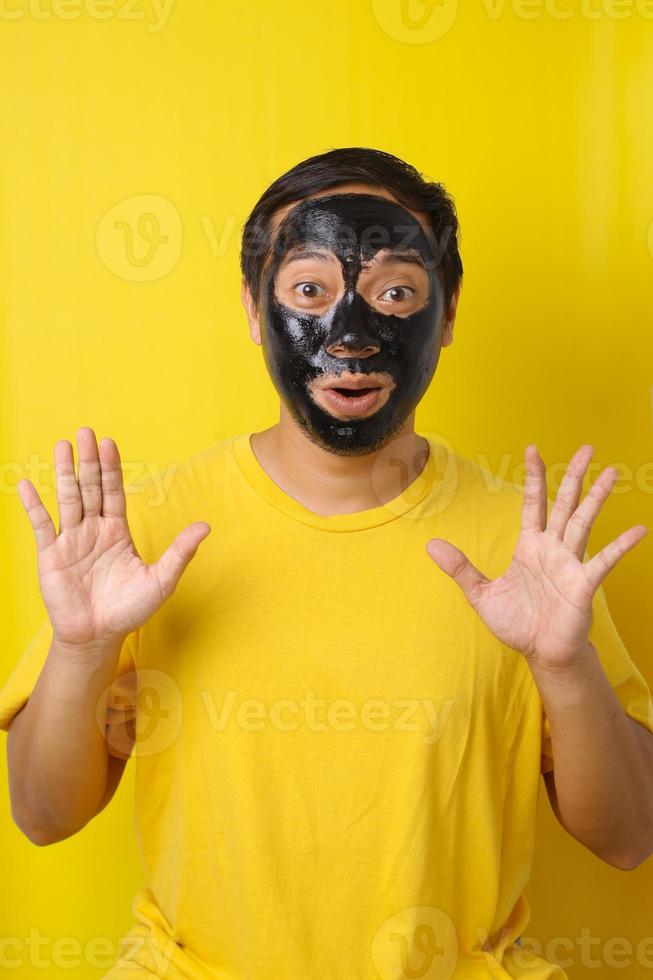 Man with cosmetics mask on the face on yellow background. Photo of man with perfect skin. Beauty and Skin care concept, funny gesture