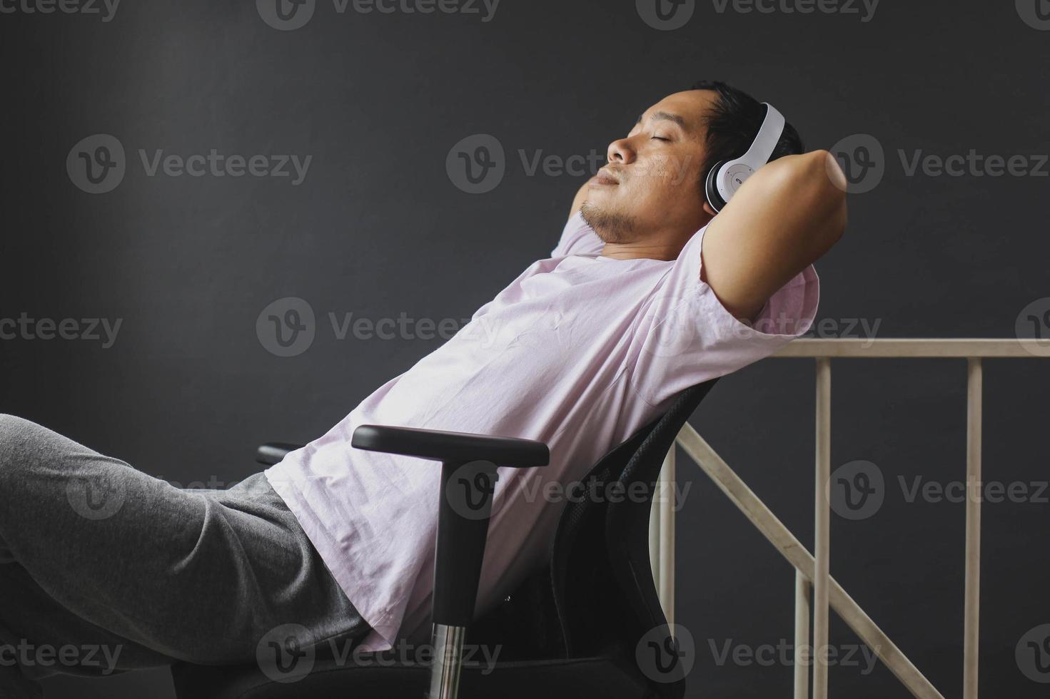 Handsome young asian man sitting relaxed closing his eyes enjoying songs via headphones in apartment photo