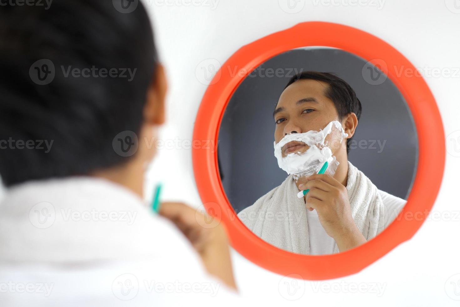 Mature handsome Asian man shaving in front of mirror photo