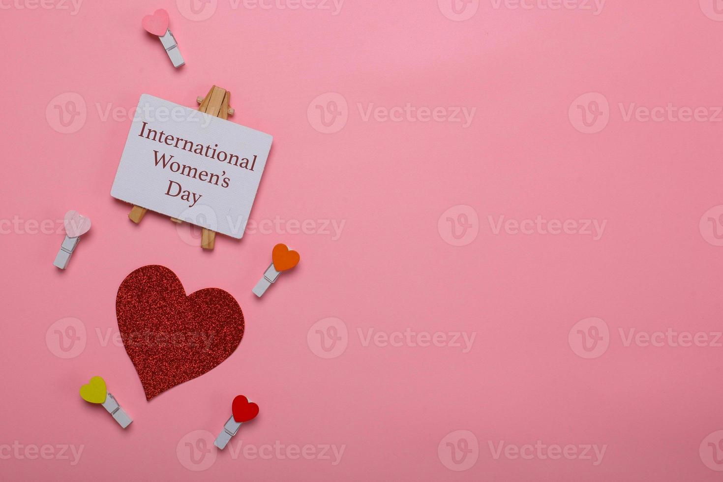 Flat lay view of international women's day signboard with sparkling and mini hearts on clothespin on pink background photo