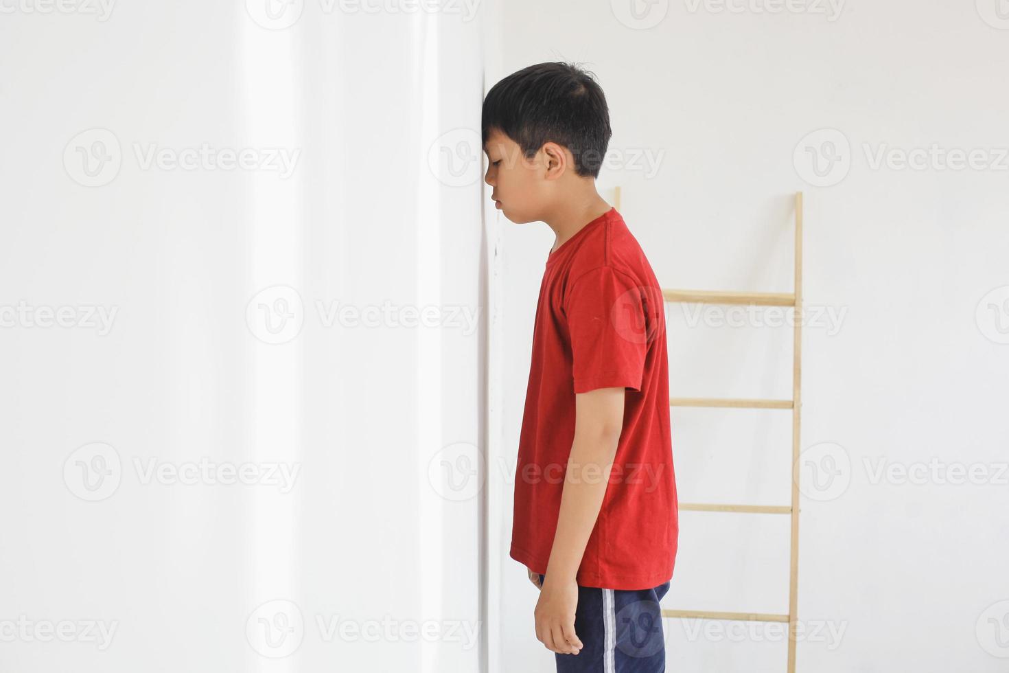 Kid standing in front of the wall because of being punished by the parents, the kid feel sad. photo