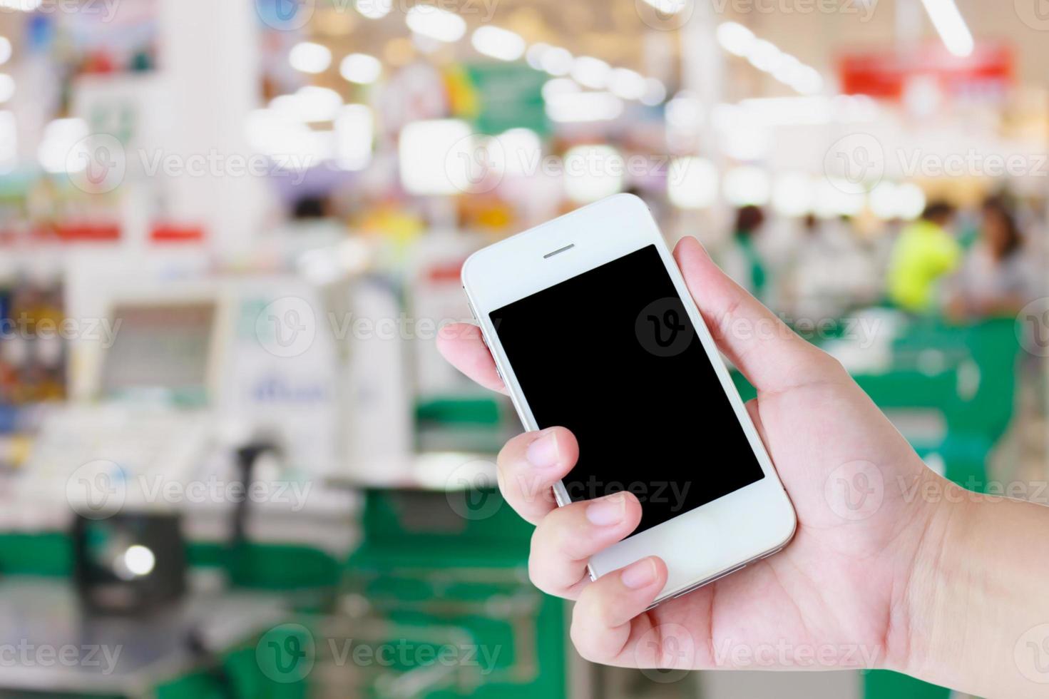 mano que sostiene el teléfono móvil en el fondo de la caja del supermercado foto