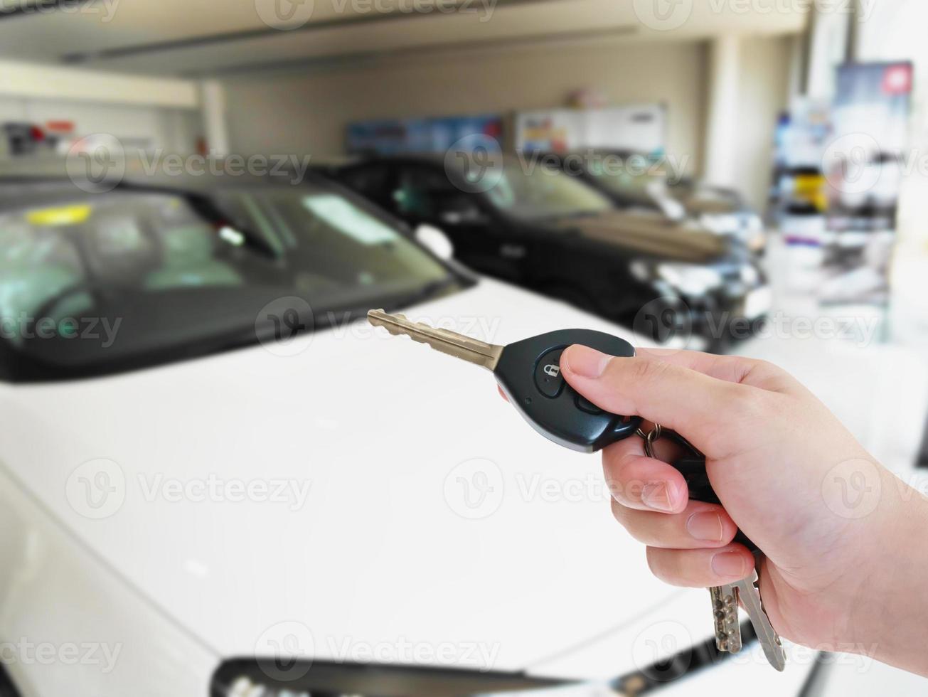 Sostenga la llave del coche con la sala de exposición de coches borrosos foto