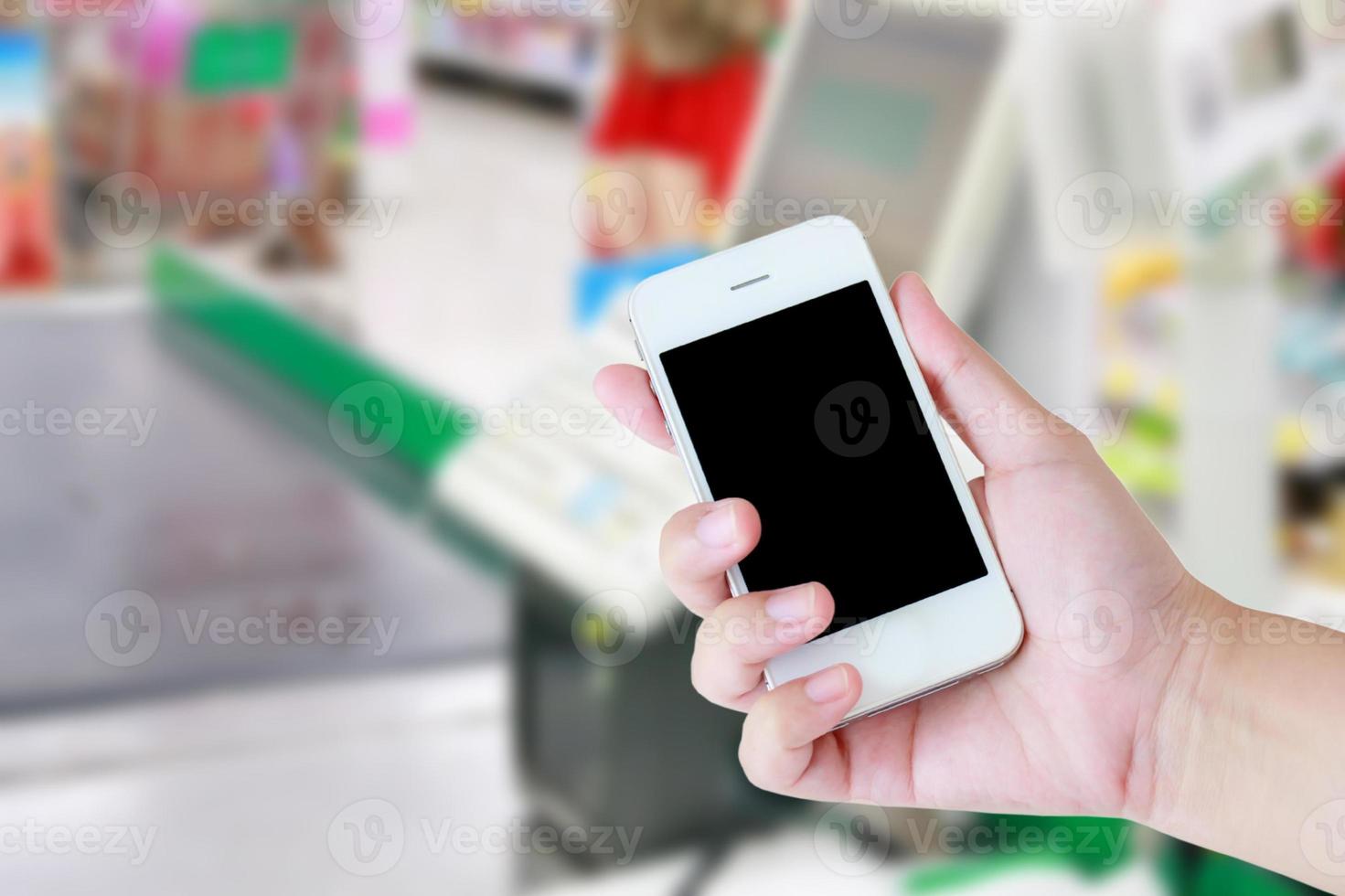 Hand holding mobile phone at supermarket checkout background photo