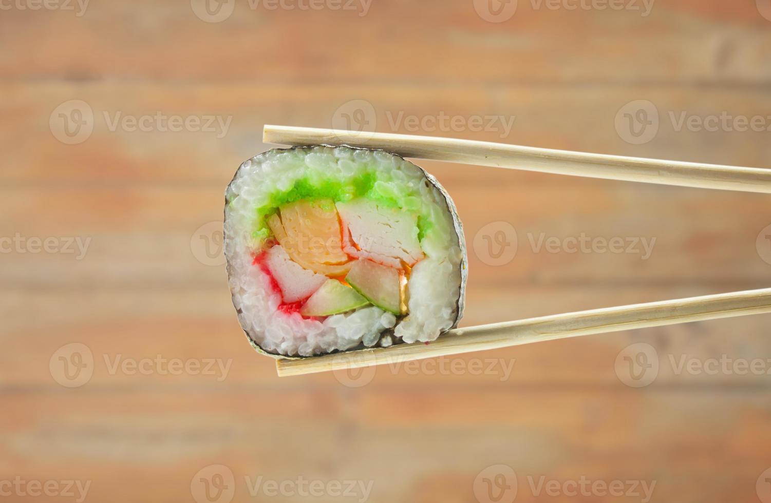 rollo de sushi con palillos sobre fondo de madera foto