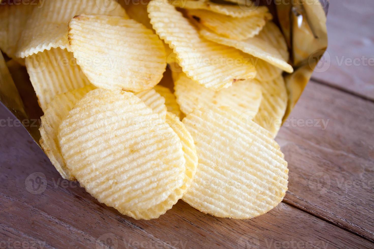 Opened pack with potato chips over wooden table photo