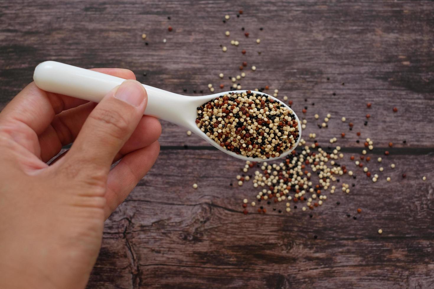 Close up hand holding the white soup spoon with quinoa seeds on wooden table background. Quinoa is a good source of protein for people following a plant-based diet. Top view. photo