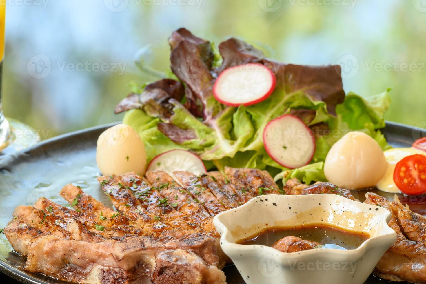 Roasted steak pork, grilled pork chops with vegetable salad and toast bread with steak sauce in black plate on the dining table food photo