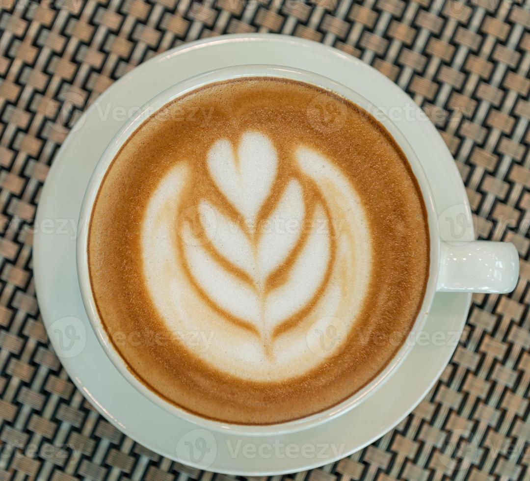 Latte art coffee cup on glass table. Blurred leaf reflection background. photo