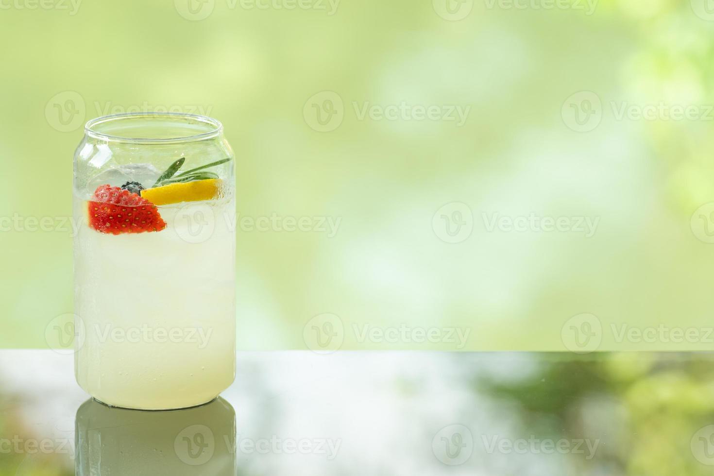Delicioso refresco de limón fresco y jugoso en la mesa de vidrio fondo de reflexión de hoja borrosa foto