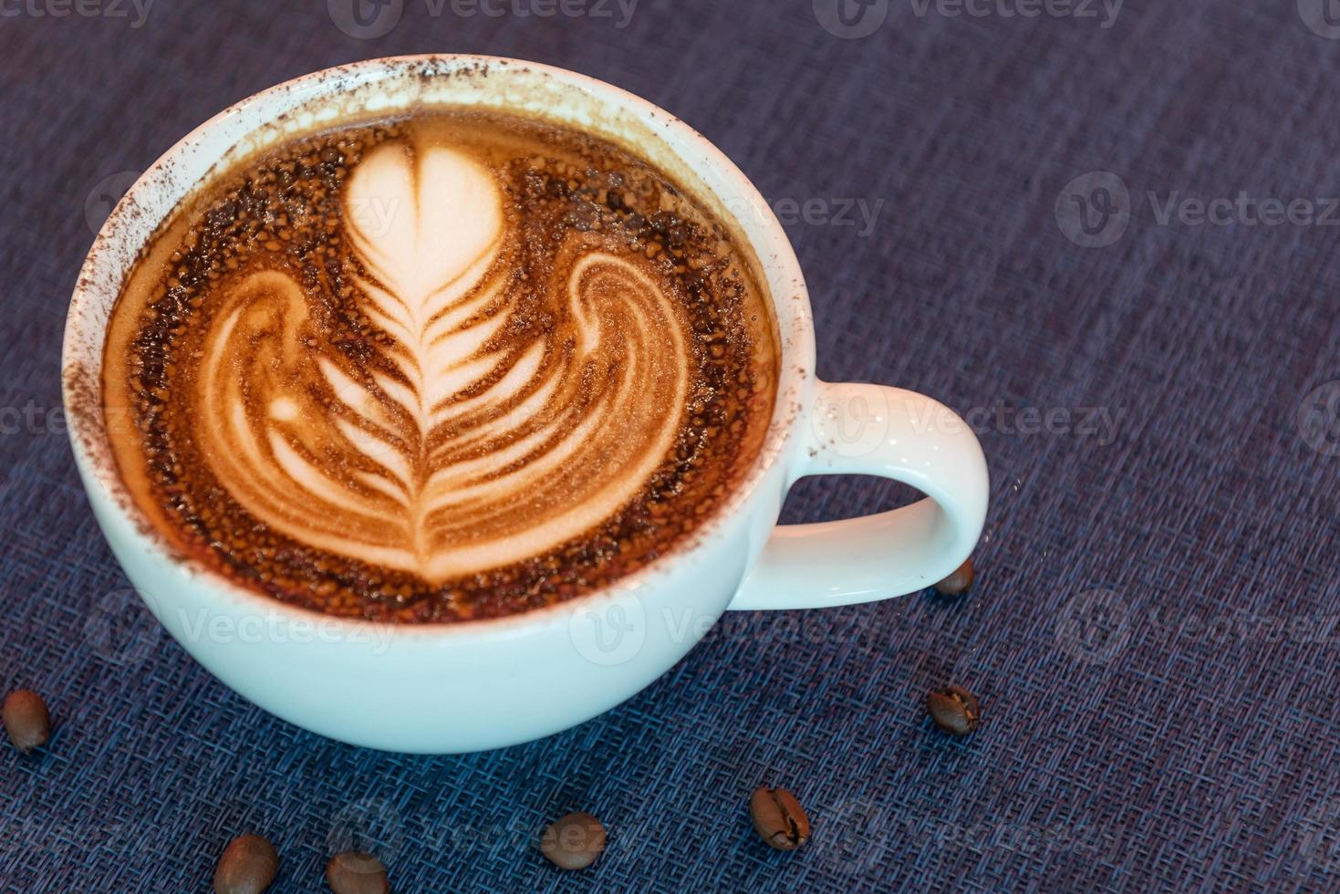 Latte art coffee cup on glass table. Blurred leaf reflection background. photo