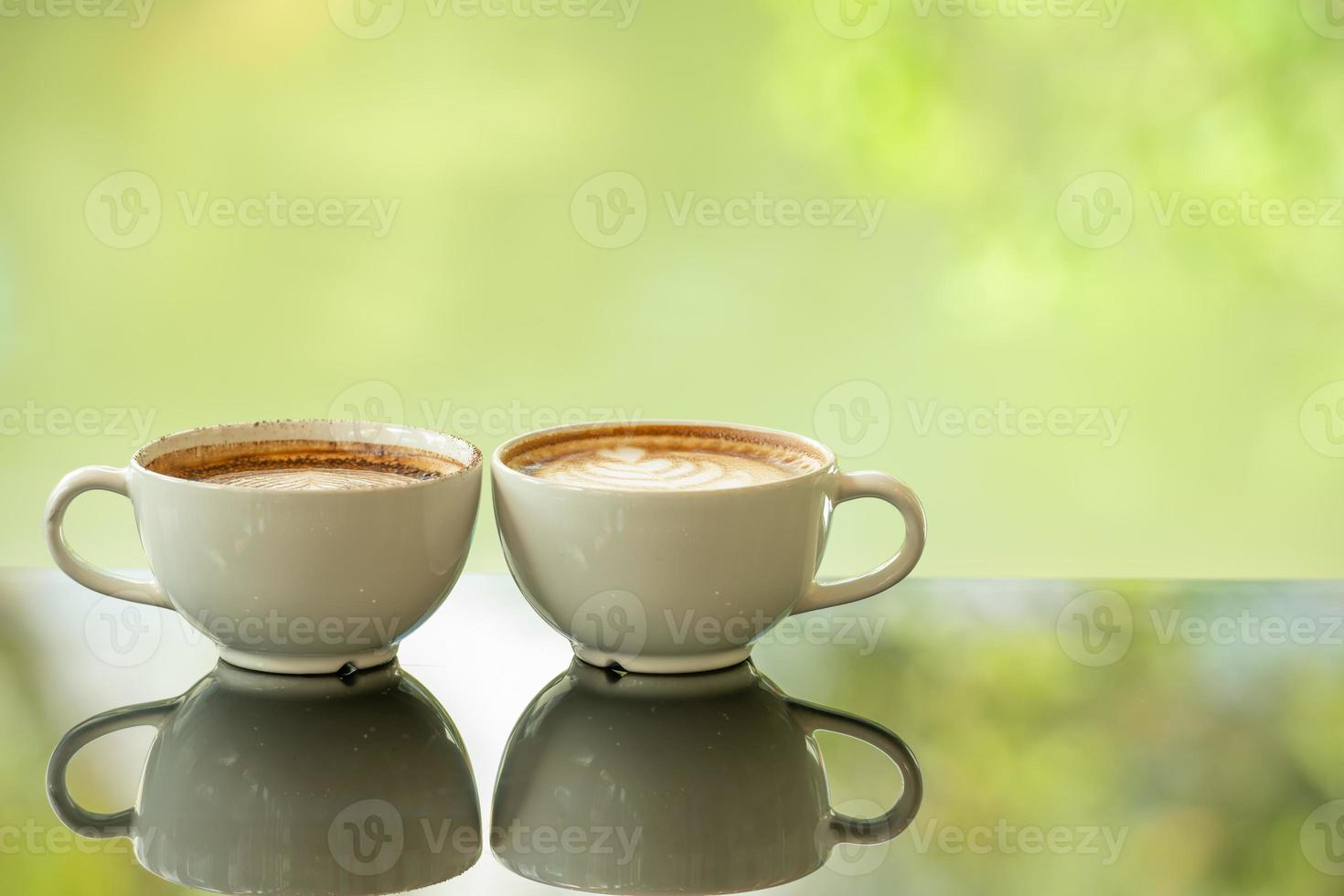 Latte art coffee cup on glass table. Blurred leaf reflection background. photo