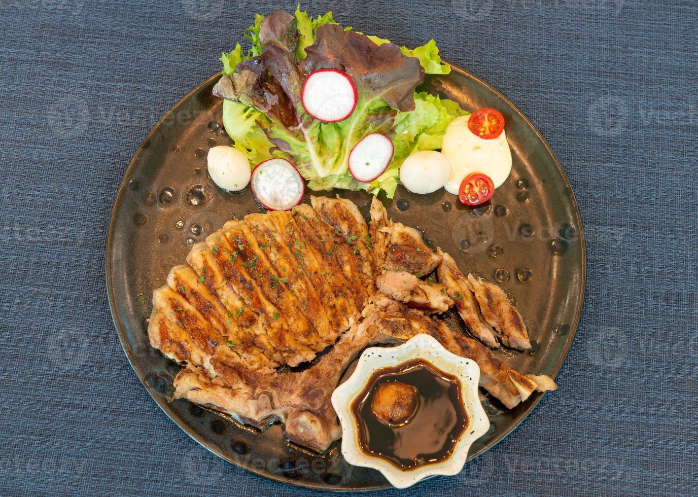 Roasted steak pork, grilled pork chops with vegetable salad and toast bread with steak sauce in black plate on the dining table food photo