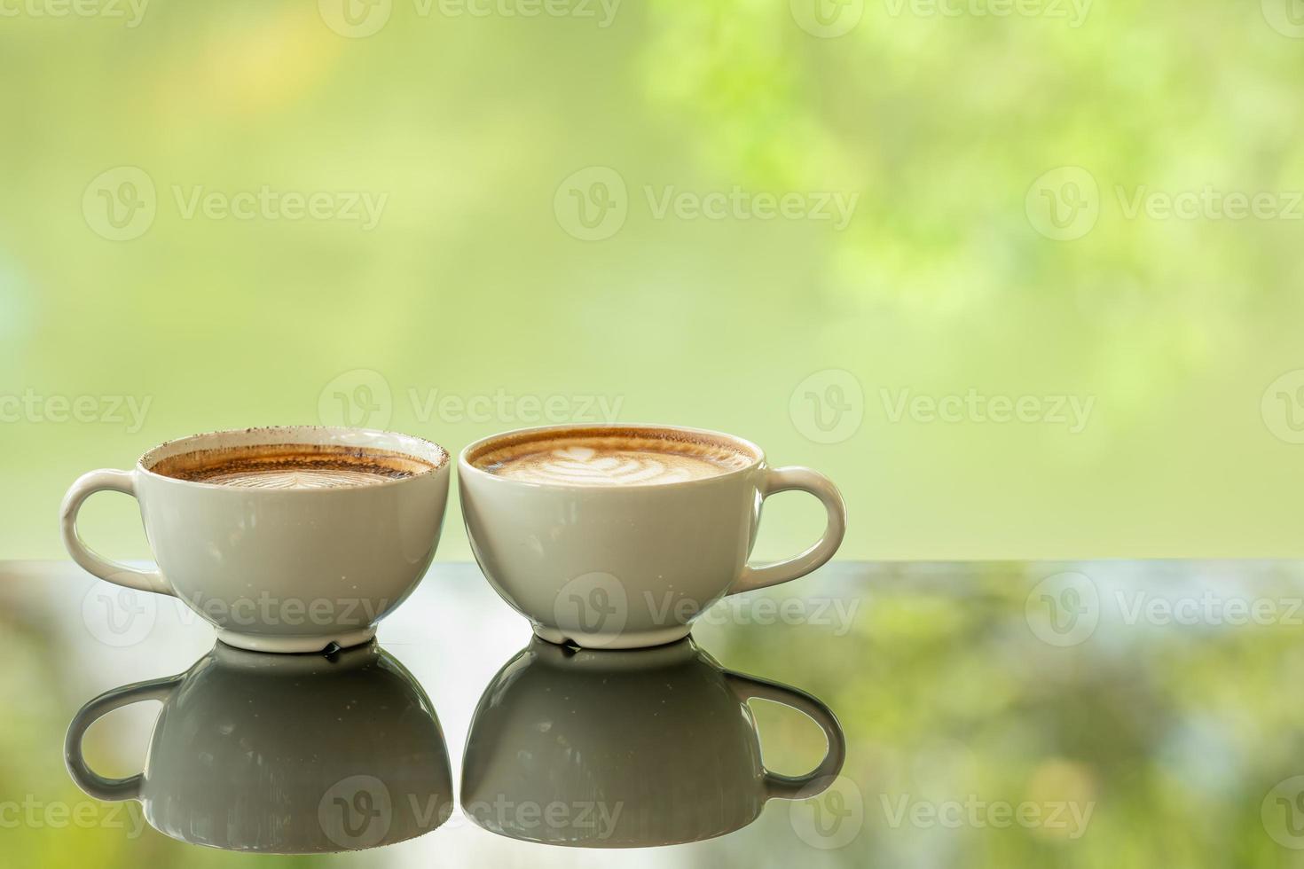 Latte art coffee cup on glass table. Blurred leaf reflection background. photo