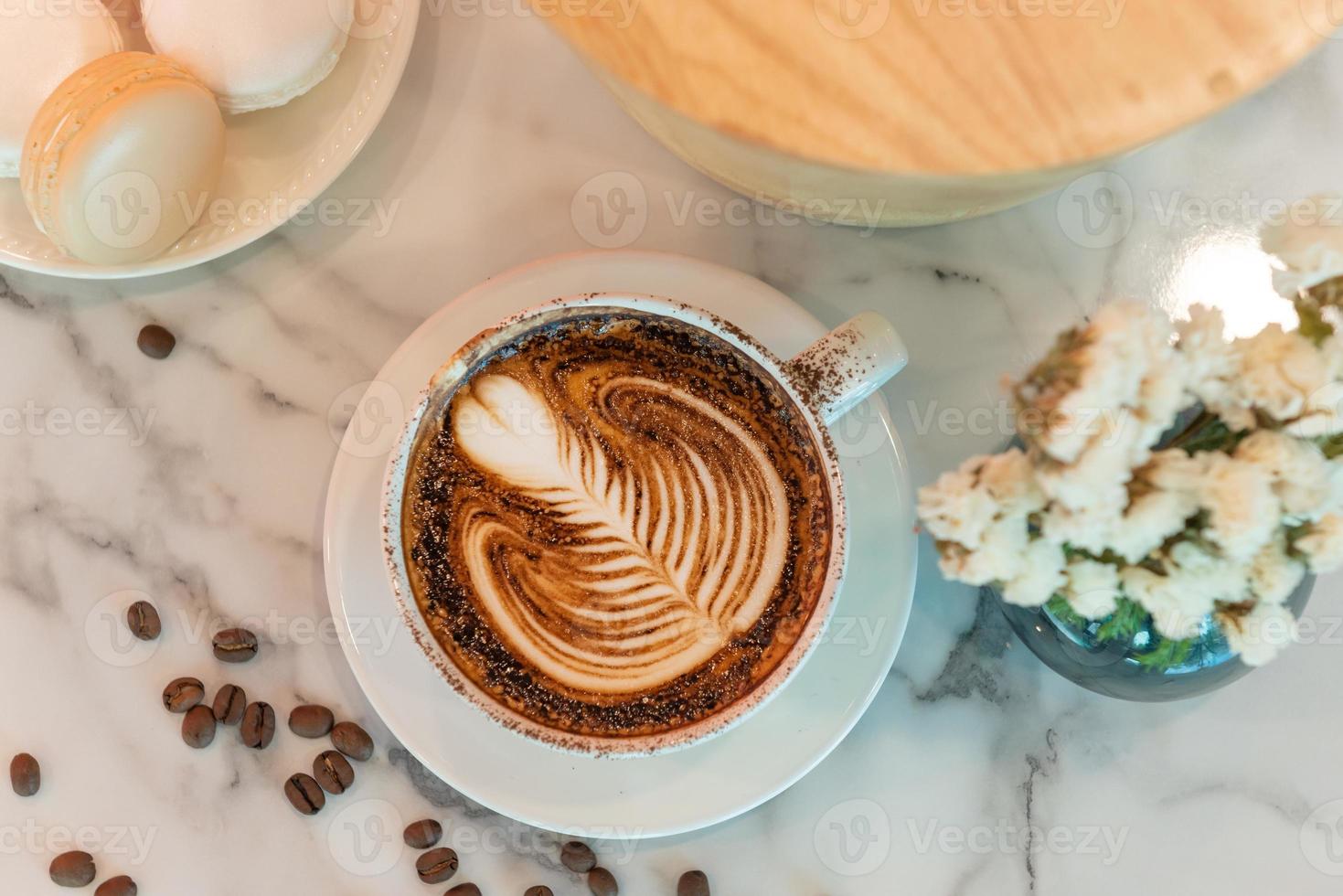 Latte art coffee cup on glass table. Blurred leaf reflection background. photo