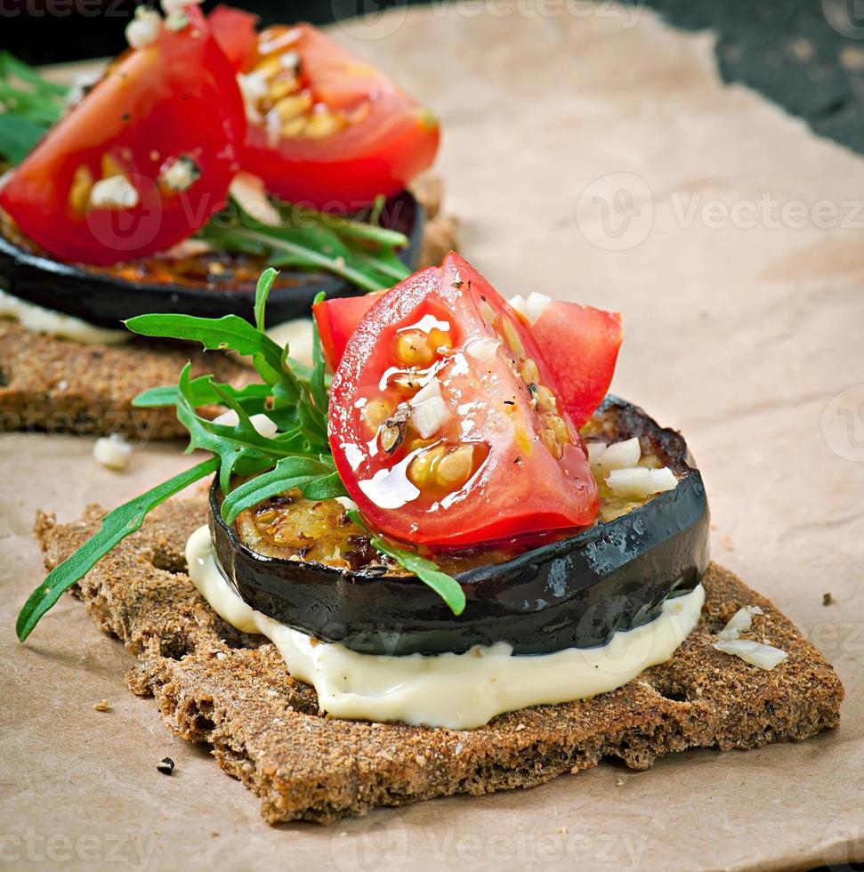 Sándwiches de pan crujiente de dieta vegetariana con queso crema de ajo, berenjena asada, rúcula y tomates cherry sobre fondo de madera vieja foto