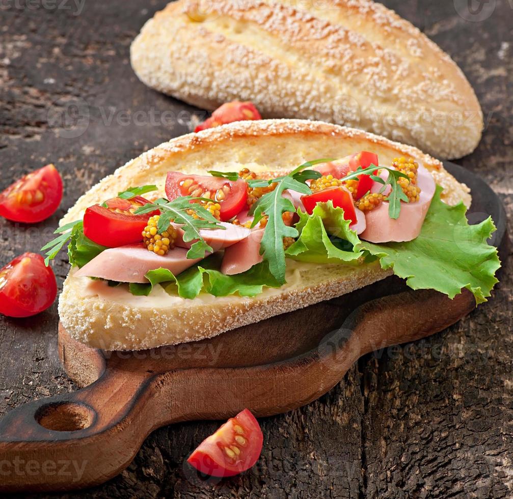 Sandwich with sausage, lettuce, tomato and arugula on the old wooden background photo