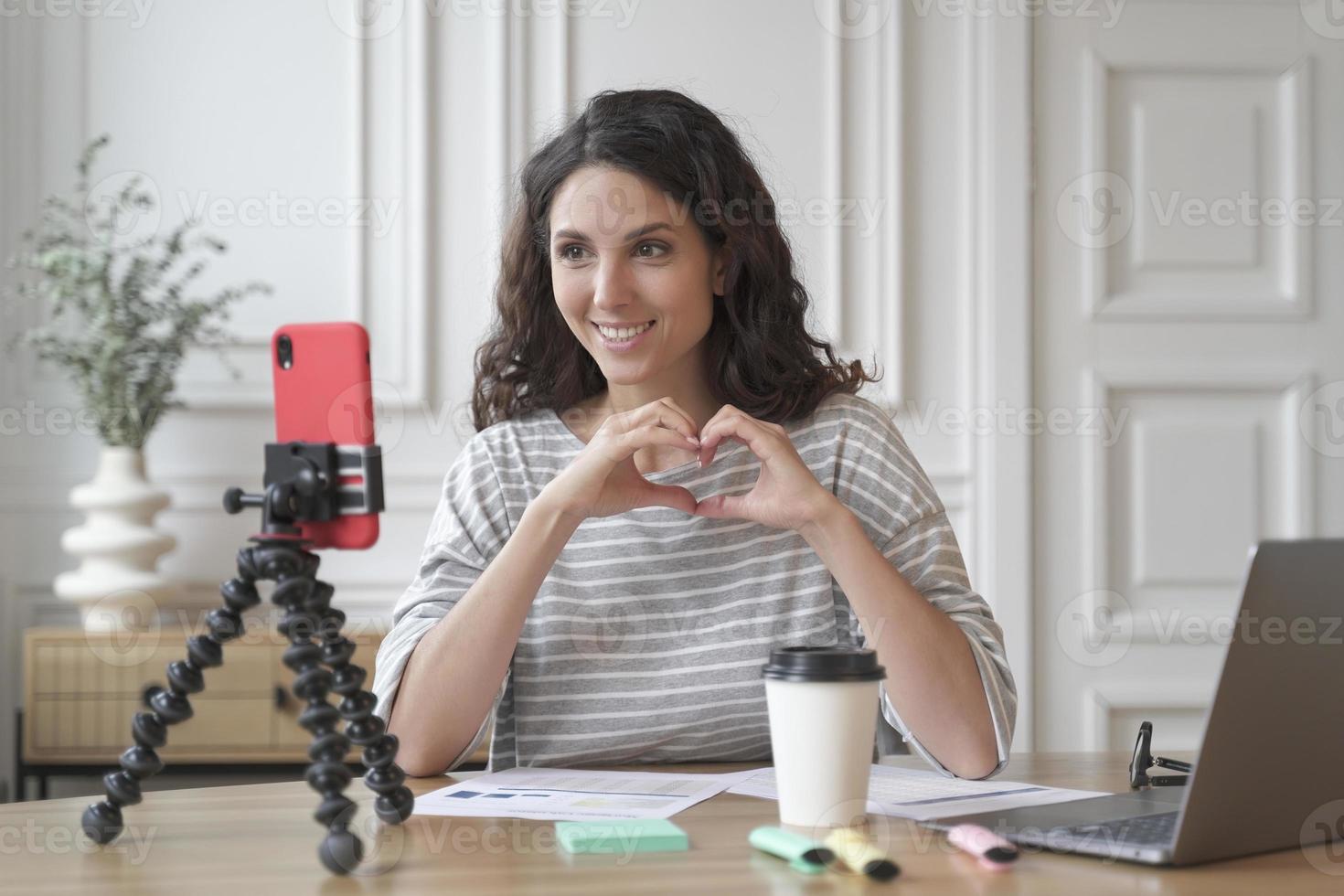 Young pleasant Italian woman blogger influencer sitting in front of smartphone and shooting video photo