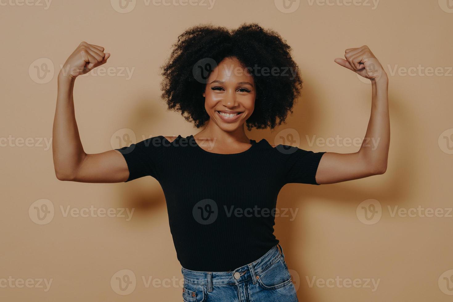 Young confident african lady in casual clothes showing strength of her arms by lifting them up photo