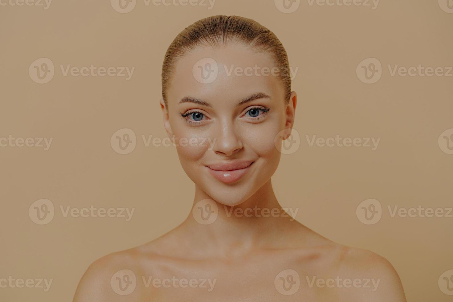 Beauty portrait of charming woman with healthy glowing skin posing seminude against beige wall photo