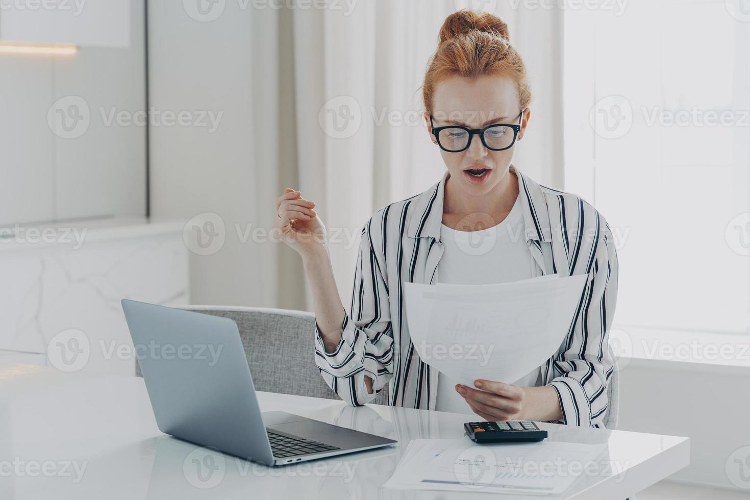 Savings finances concept. Shocked ginger woman focused at document studies bills reads banking paper photo