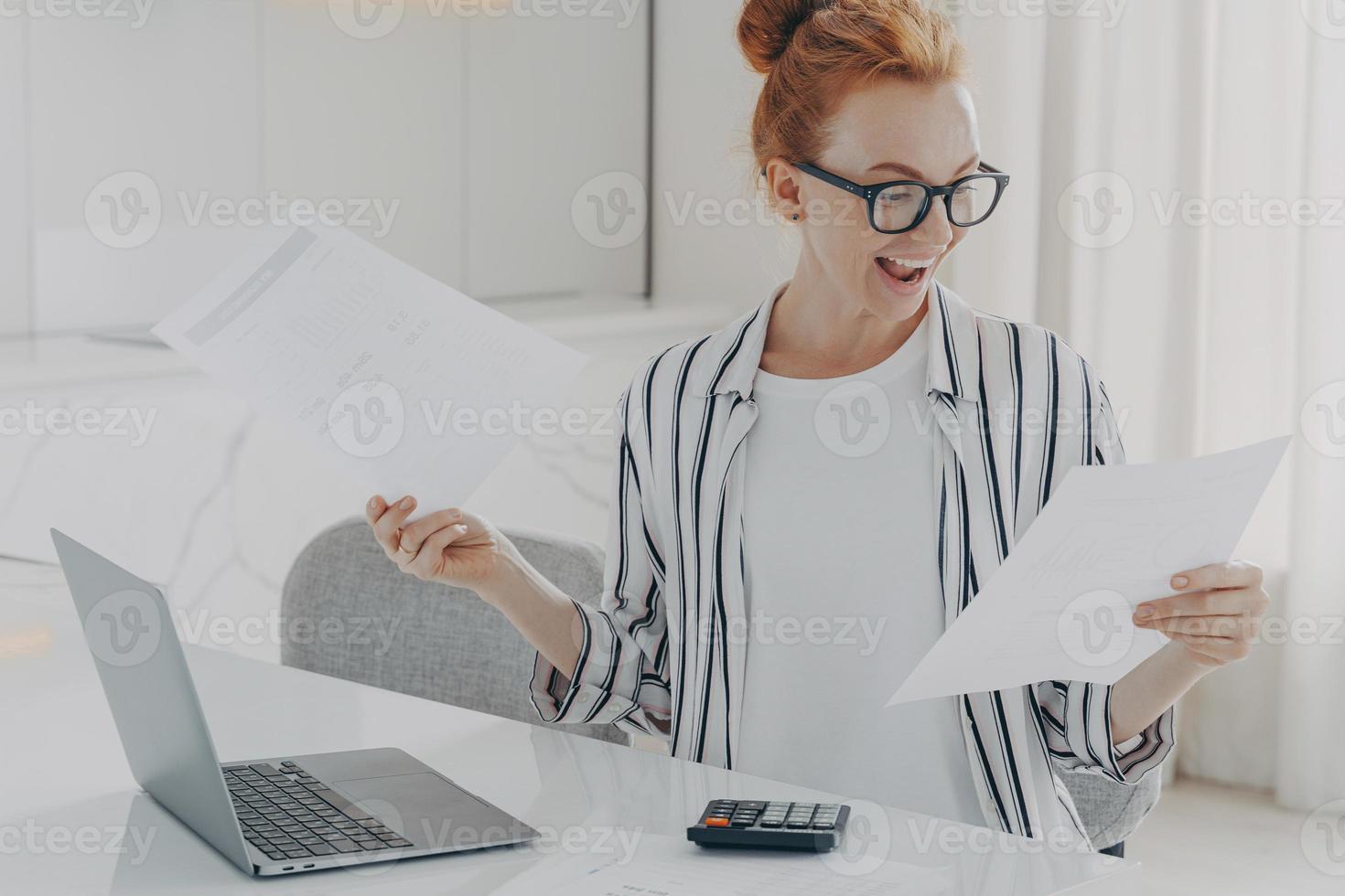 Positive young woman with red hair calculates utility charges engaged in planning monthly budget photo