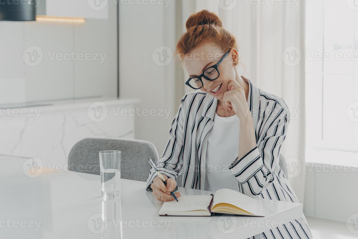 European woman makes notes in personal planner smiles gently holds pen poses at desktop photo