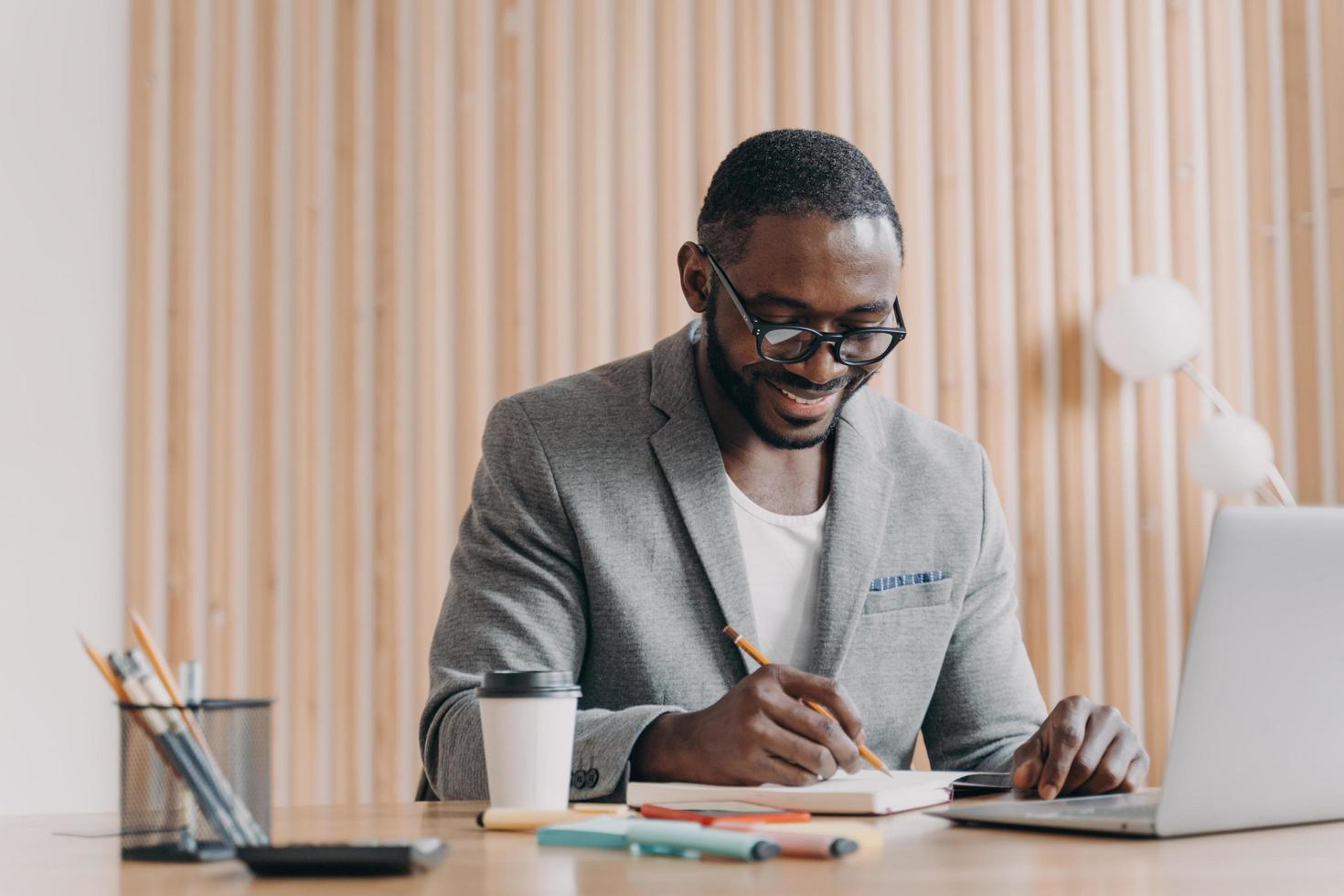Happy afro american smiling businessman makes notes in agenda while having video call online photo