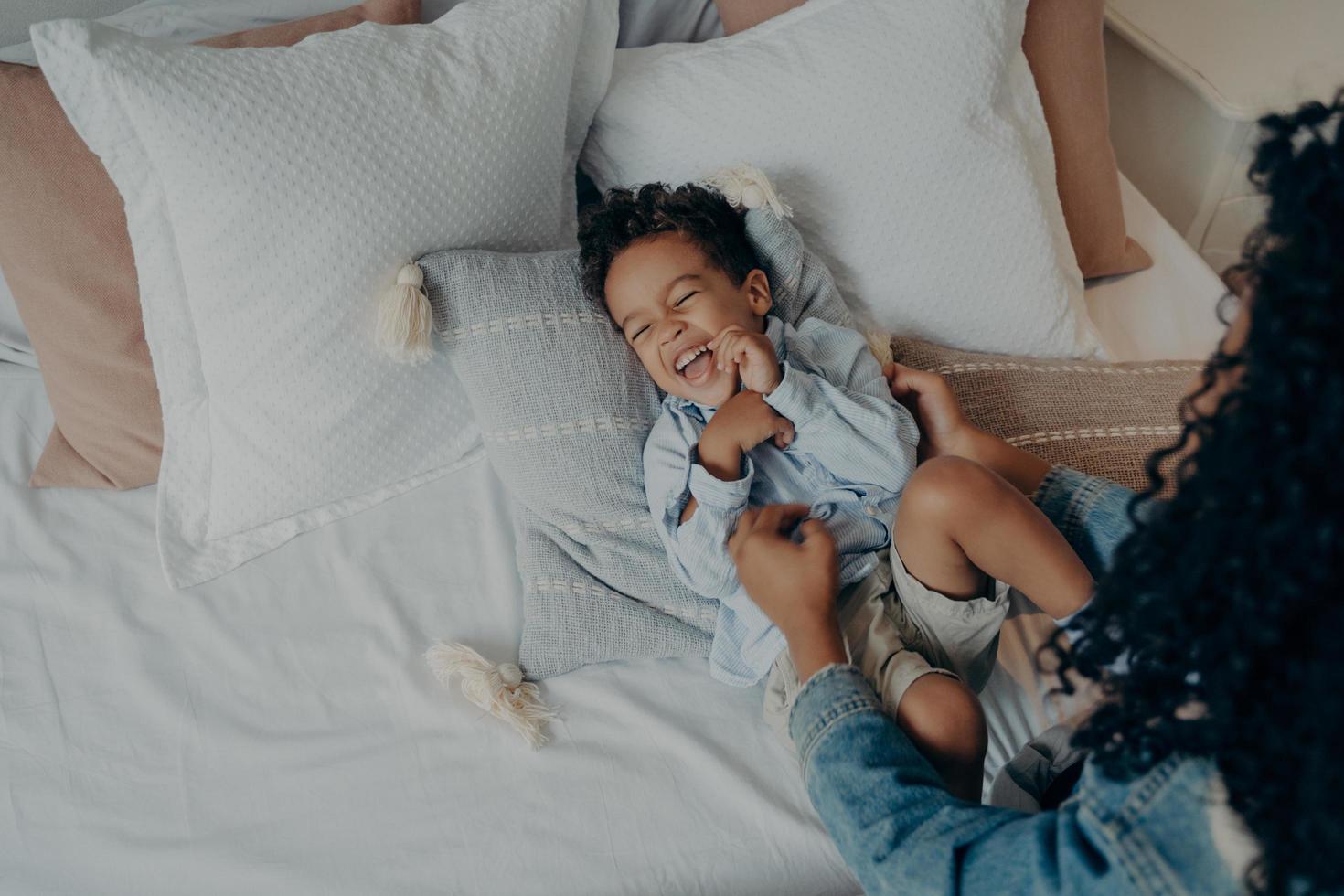 Lovely mother tickling her cute little son lying on bed and laughing photo