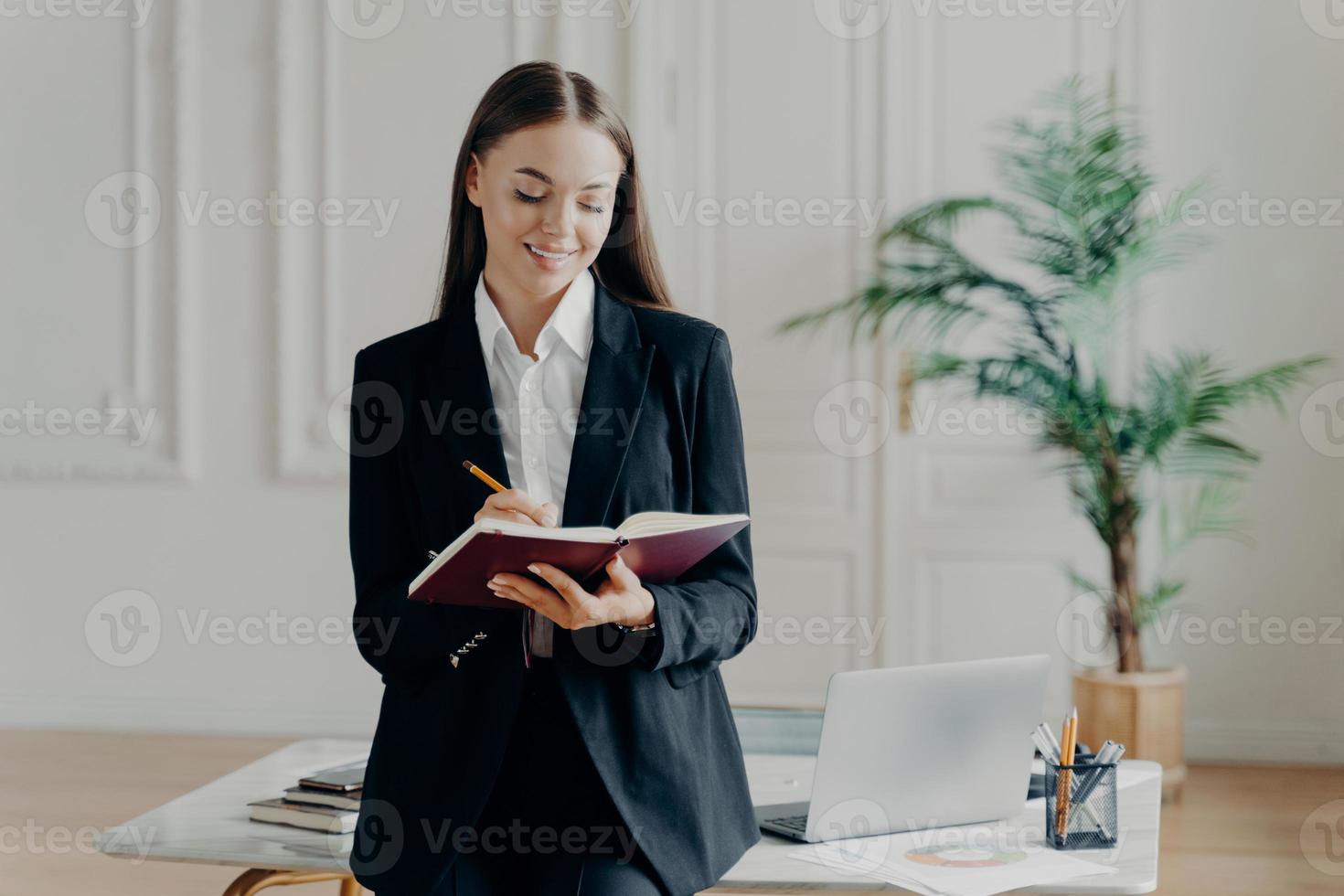 mujer de negocios feliz con traje formal negro sosteniendo un cuaderno y sonriendo foto