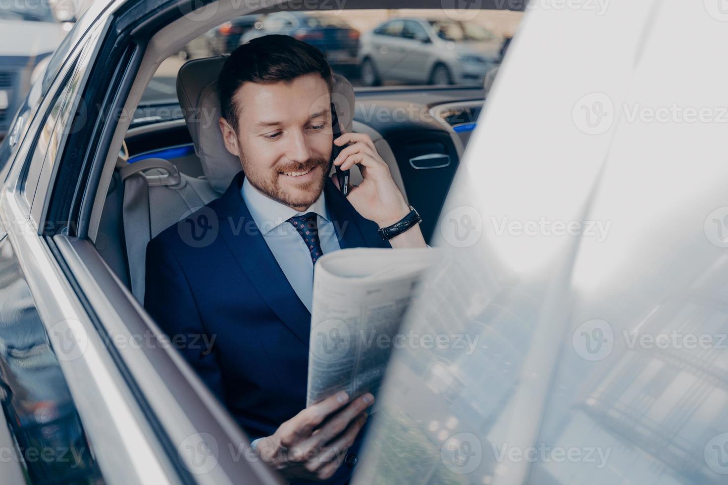 Good looking young executive manager in formal wear reads newspaper on backseat of car photo