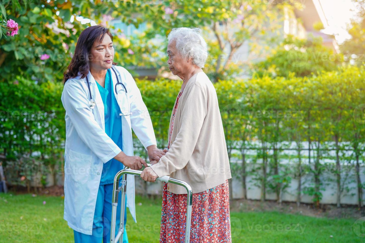 el médico ayuda a una anciana asiática con discapacidad a caminar con un andador en el parque, concepto médico. foto