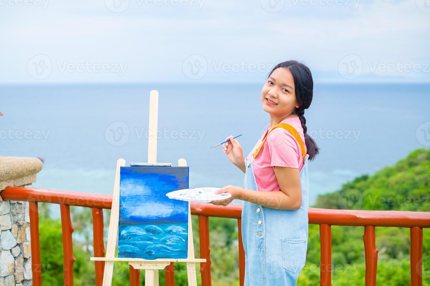 niña usando un dibujo de pincel sobre papel de lienzo, en una hermosa vista del paisaje en koh tao, tailandia. foto