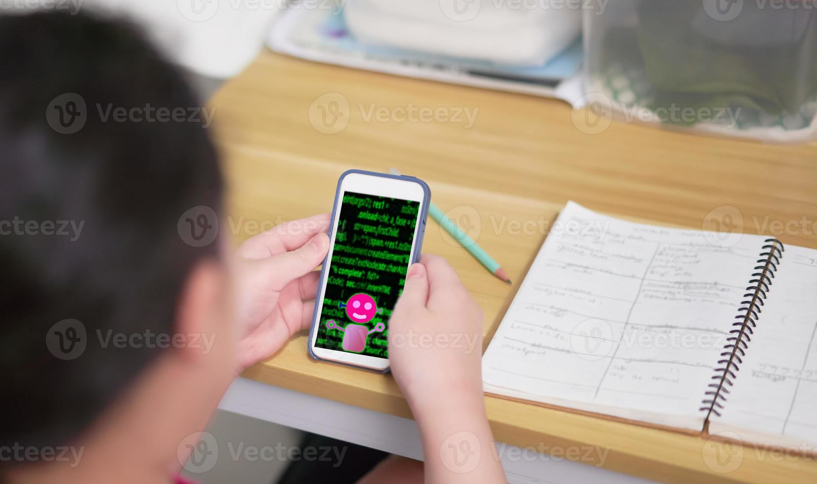 A black haired girl is using her mobile phone to search for information. doing homework on the table at home photo