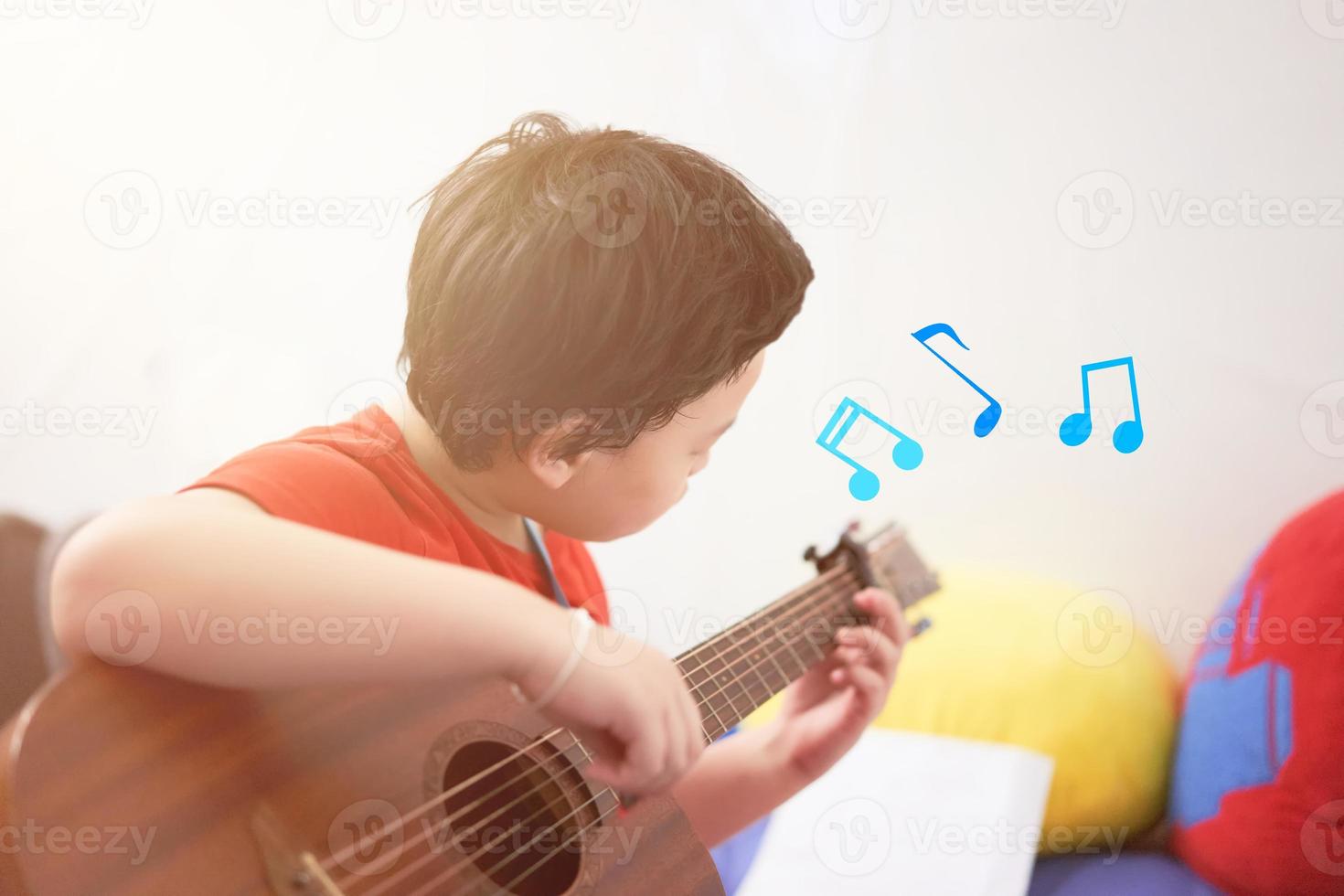 The boy plays the guitar with his left hand, a song by himself, on the sofa, in the bedroom, reading the sheet music. photo