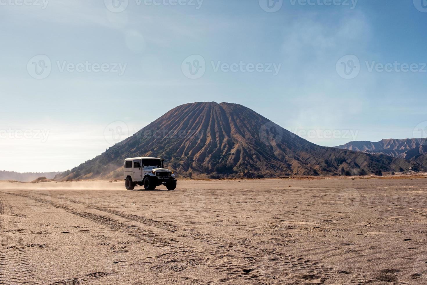 White four-wheel driving on desert with volcano photo