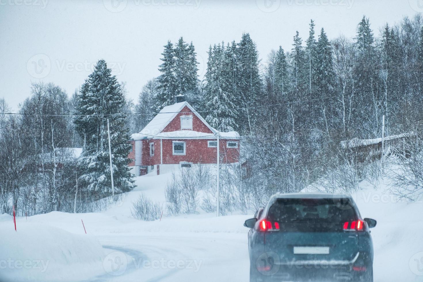 conducción de automóviles en ventisca con casa roja en el campo en invierno foto
