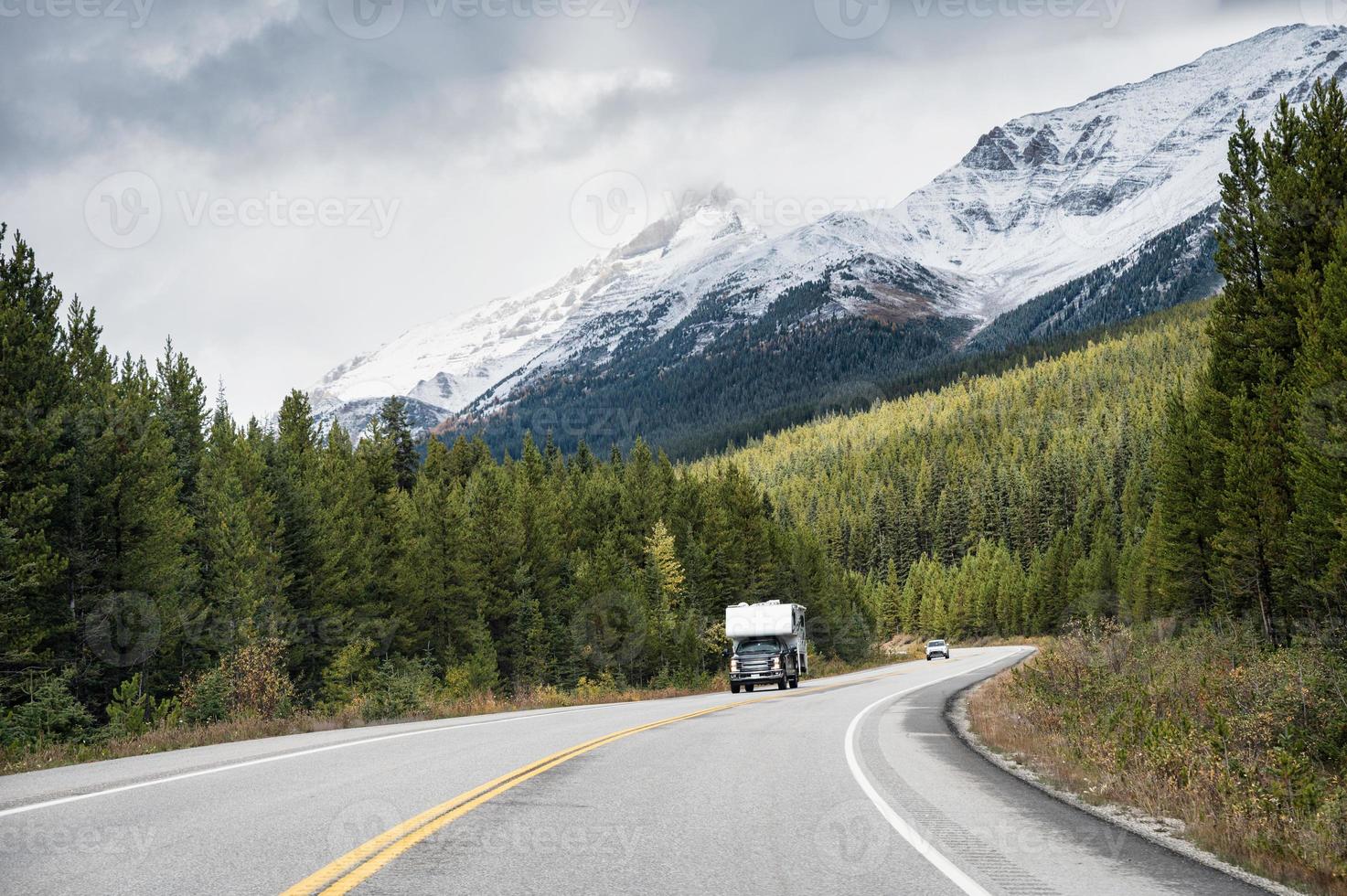 viaje por carretera de una autocaravana conduciendo por una carretera con montañas rocosas en un bosque de pinos en el parque nacional de banff foto