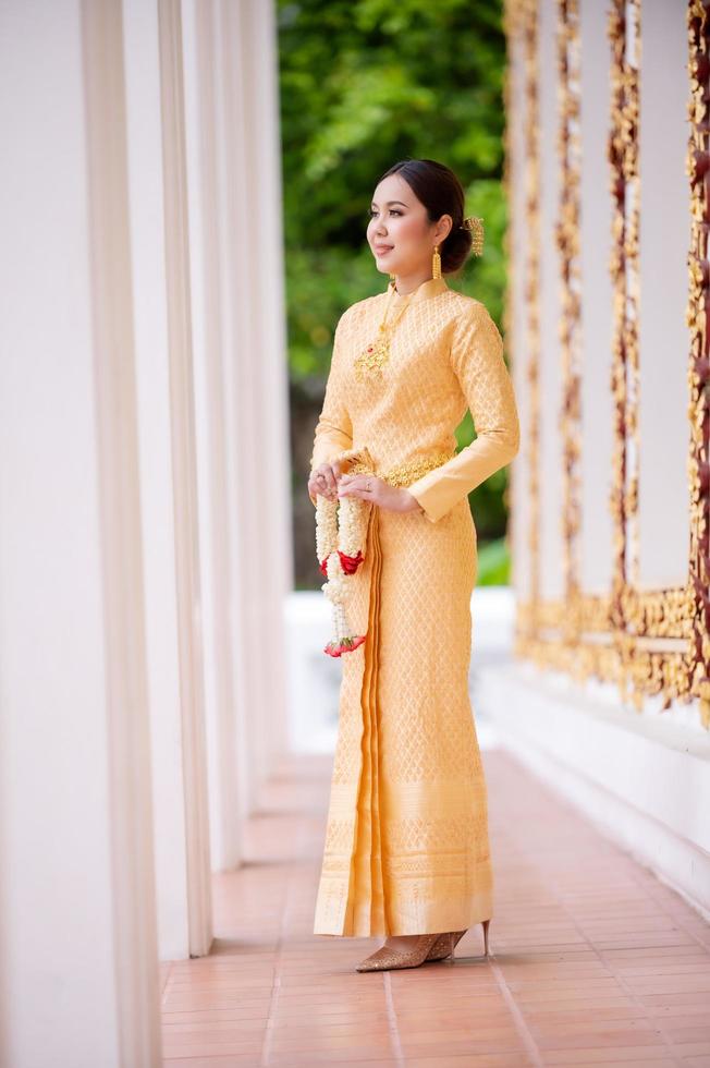 An elegant Thai woman in Thai dress adorned with precious jewelry holds a flower garland in a beautiful ancient Thai temple photo